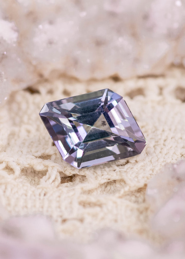 Natural 1.52 carat Tanzanite gemstone on crocheted fabric showing teal blue green purple hues and custom rhombus step cut facets