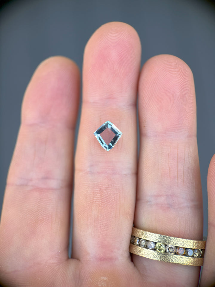 Unheated Montana sapphire held on fingertips, showing geometric shield portrait cut and vibrant teal color in daylight.