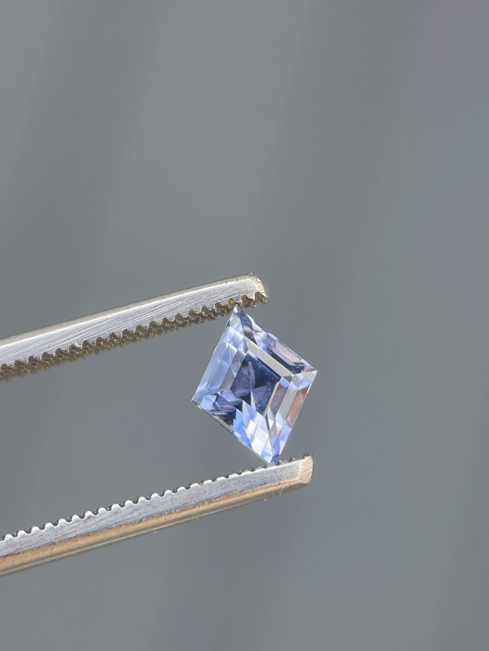 Violet and blue 1.53 carat kite step-cut sapphire held in tweezers. Showcasing precision craftsmanship and ethical sourcing from Sri Lanka.