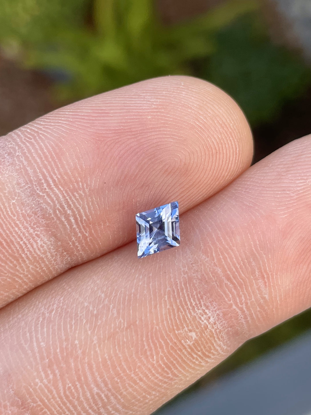 1.53 carat violet and blue kite step-cut sapphire from Sri Lanka, placed on a finger for size reference. Ethically sourced with no treatment.