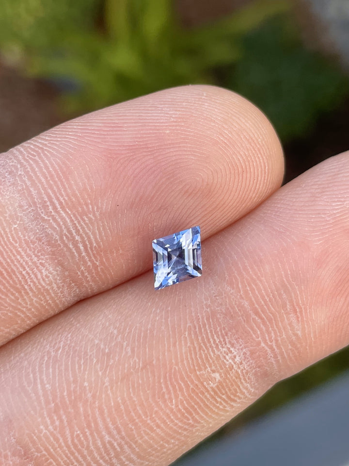 1.53 carat violet and blue kite step-cut sapphire from Sri Lanka, placed on a finger for size reference. Ethically sourced with no treatment.