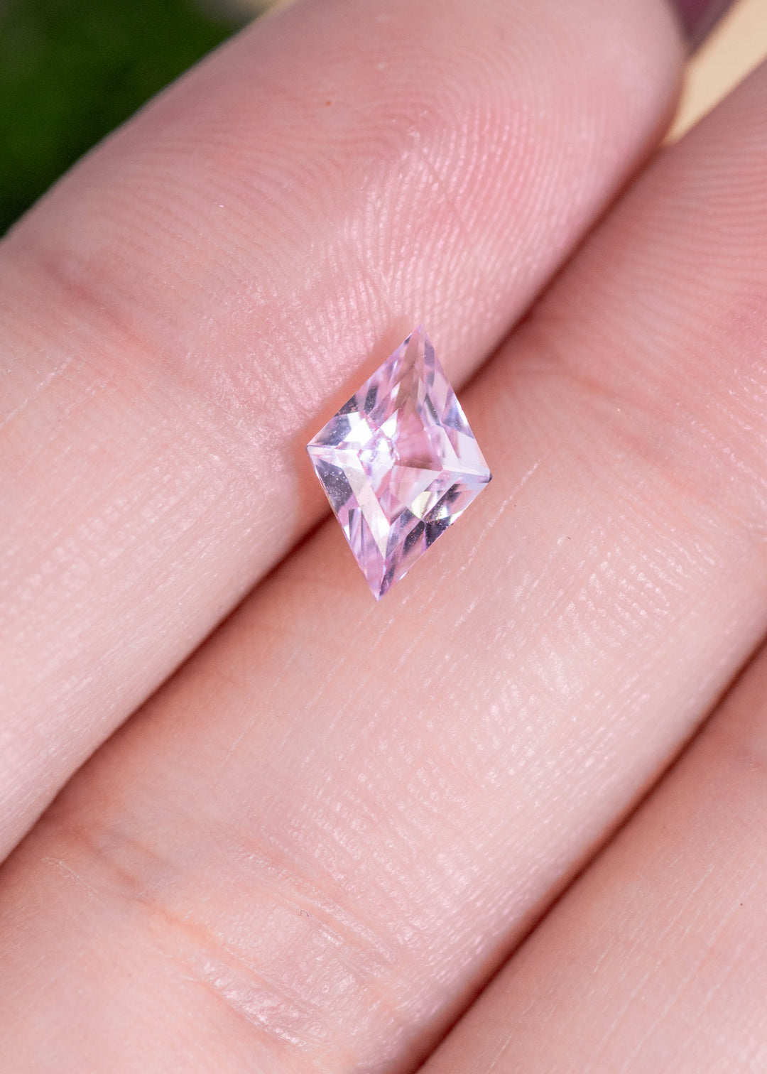 Loose blush pink sapphire resting on fingertips showing the kite step cut and delicate pink color shifting in natural light.