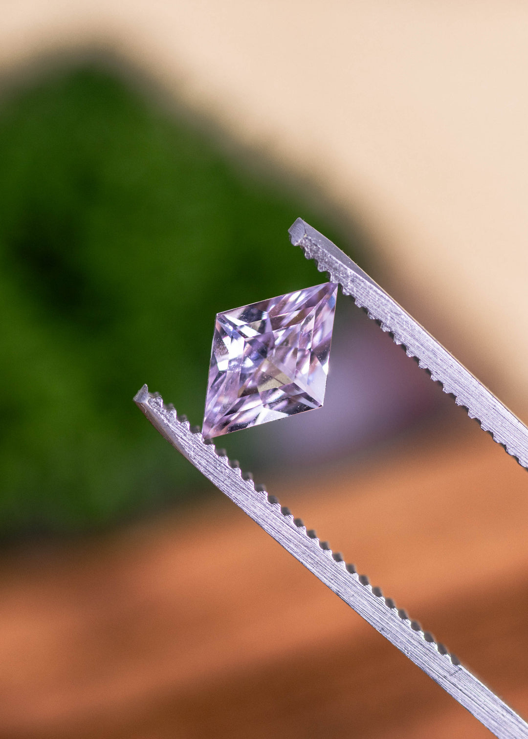 Loose blush pink sapphire from Sakaraha Madagascar held in tweezers highlighting the geometric kite step cut and light pink tones.