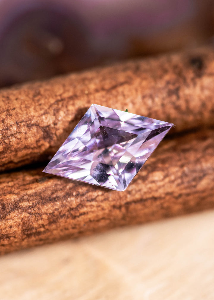 Loose blush pink sapphire from Madagascar shown face-up on natural wood displaying the kite step cut and soft pastel color.