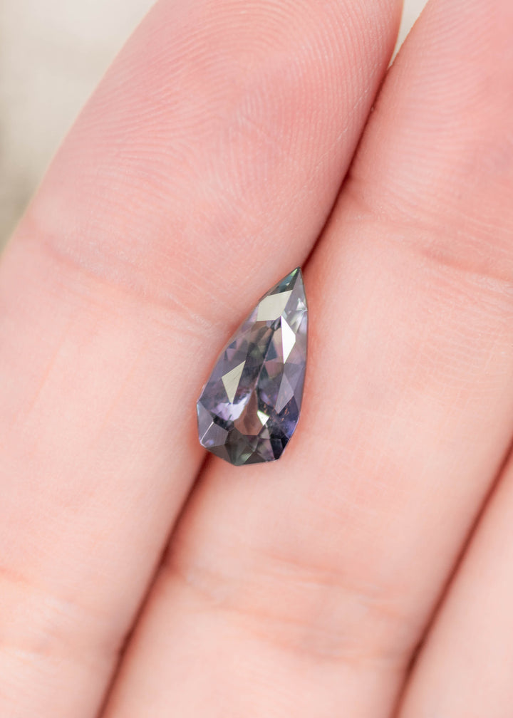 1.53 carat blue teal violet Tanzanite custom geometric pear resting on finger, precision faceted gemstone from Merelani Hills Tanzania showing trichroic color shift, brilliance and elongated designer shape for custom jewelry