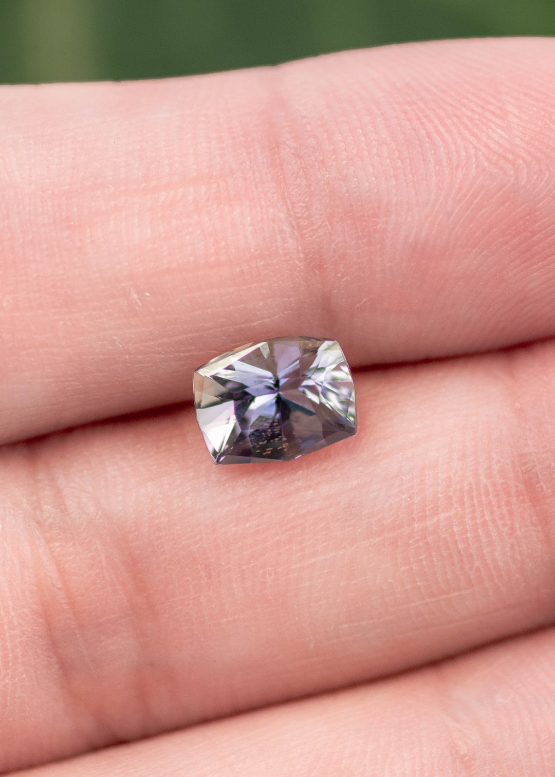 Natural 1.54CT mermaid tanzanite displayed on fingertips, highlighting the custom mix cushion cut, purple blue green hues, and untreated clarity from Merelani Hills, Tanzania.