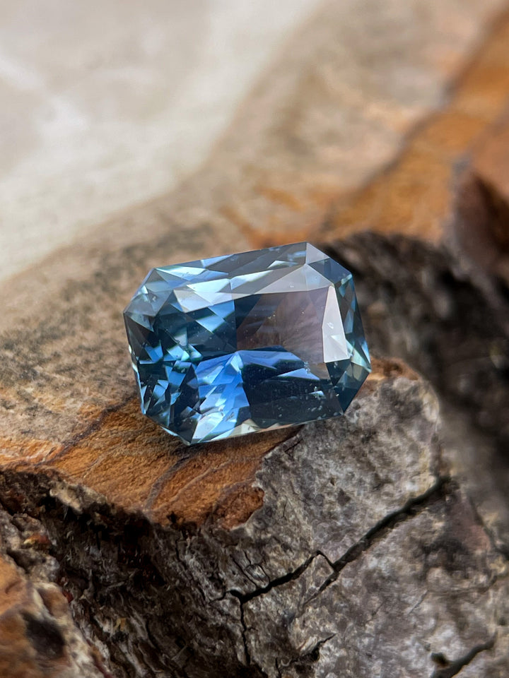 Close-up of a 1.54 carat blue sapphire radiant cut placed on textured wood, emphasizing its Sri Lankan origin and treated clarity.