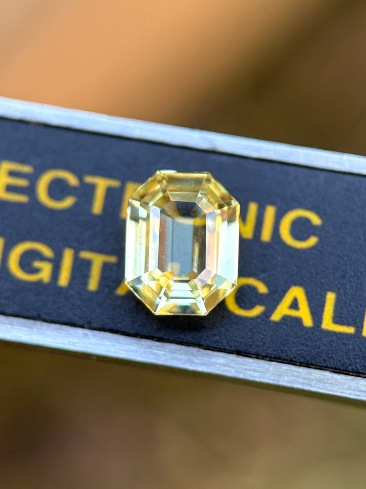 Macro photo of 1.55 carat yellow sapphire placed on digital caliper for scale, showcasing exceptional transparency, symmetry, and brilliance of the custom antidote emerald cut, untreated gemstone from Madagascar.