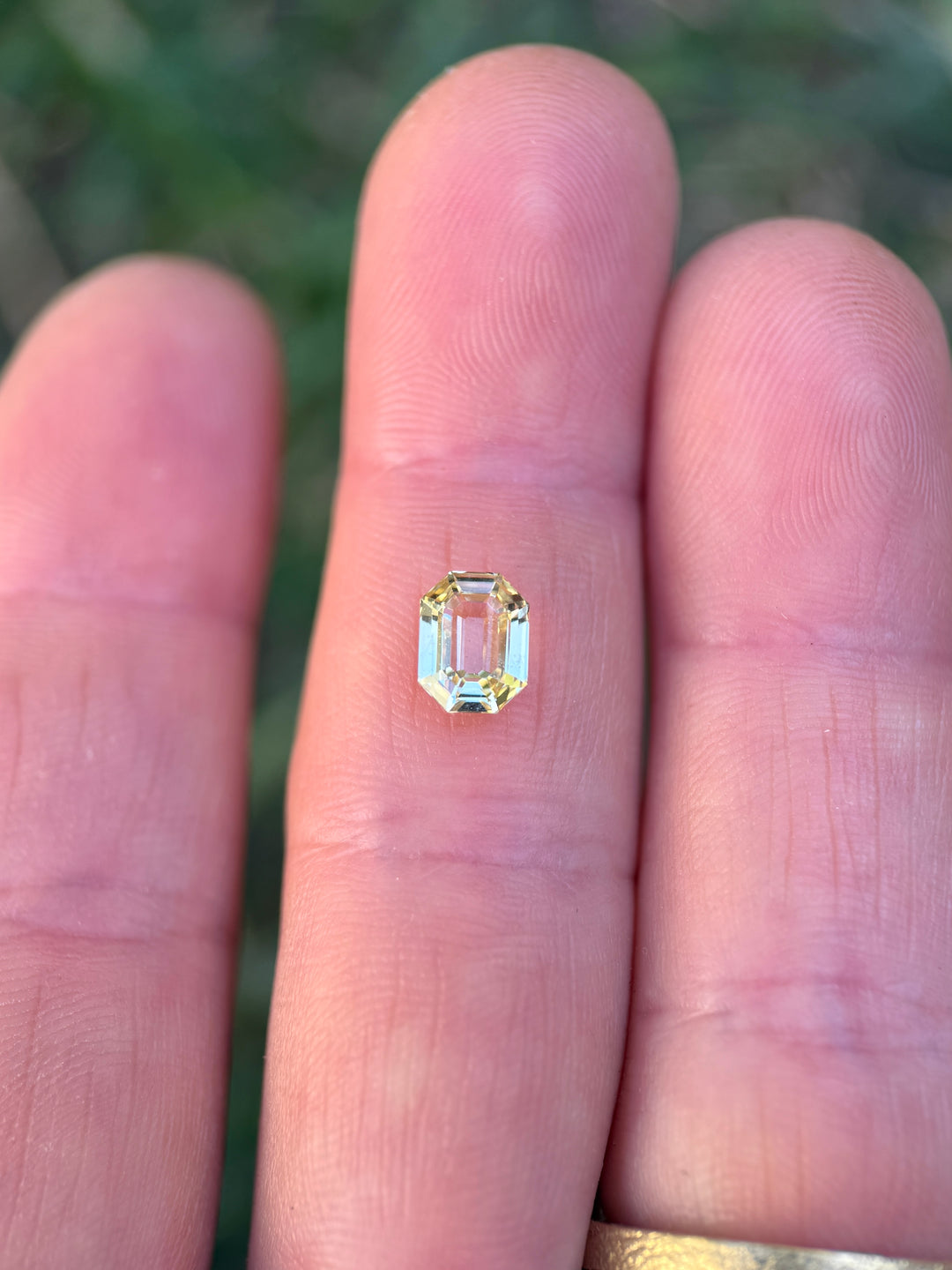 1.55CT yellow sapphire resting on fingertips, displaying its radiant golden hue, clean clarity, and reflective facets of the precision antidote emerald cut, unheated gem from Sakaraha, Madagascar.