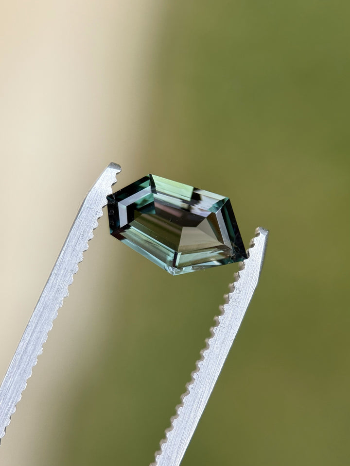 Tanzanite gemstone held in gem tweezers with a green background, revealing sharp geometric step facets and vibrant green color