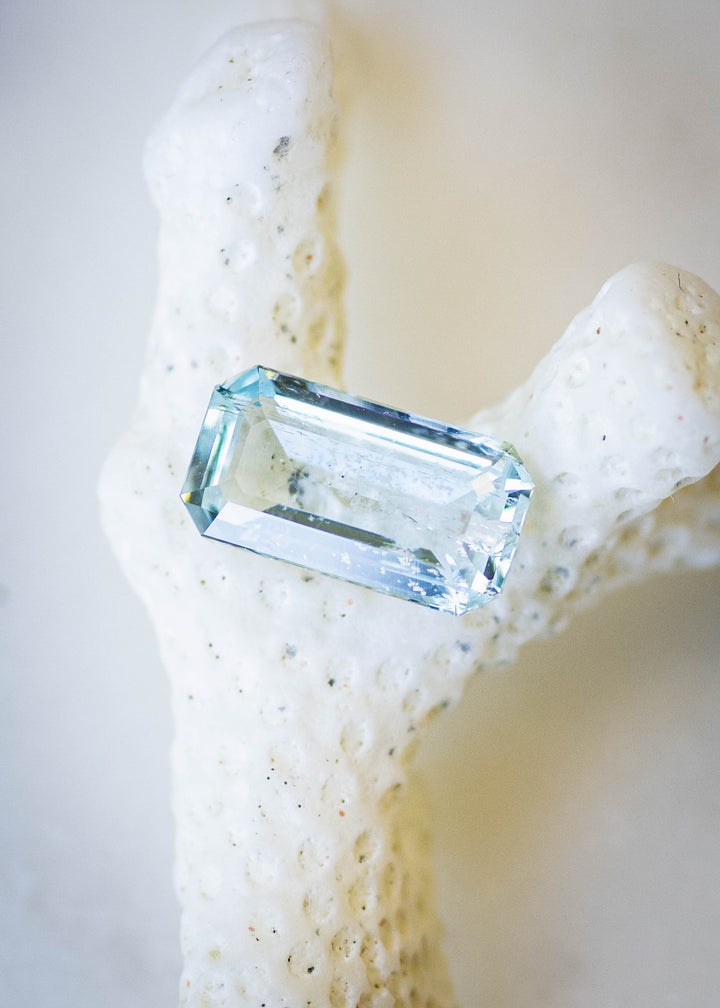 Natural untreated 1.55 carat Colorado aquamarine displayed on coral, highlighting its elongated octagonal step cut and light medium blue color.