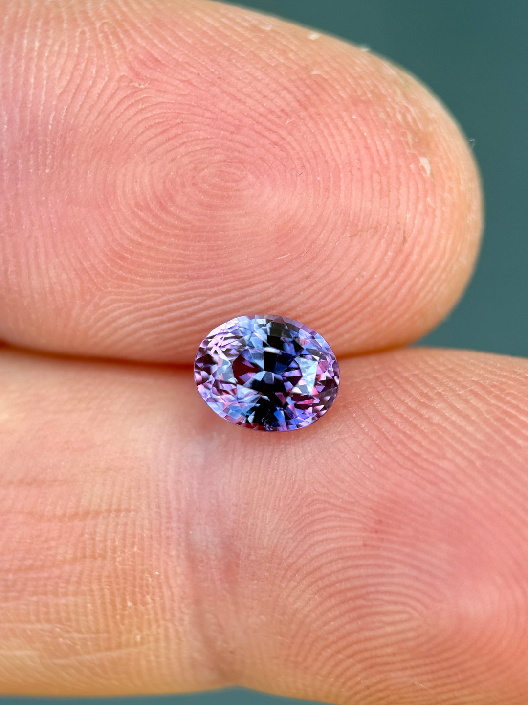 1.55ct vivid pink purple sapphire rotating in hand, revealing bright magenta flashes and precision oval cut brilliance.