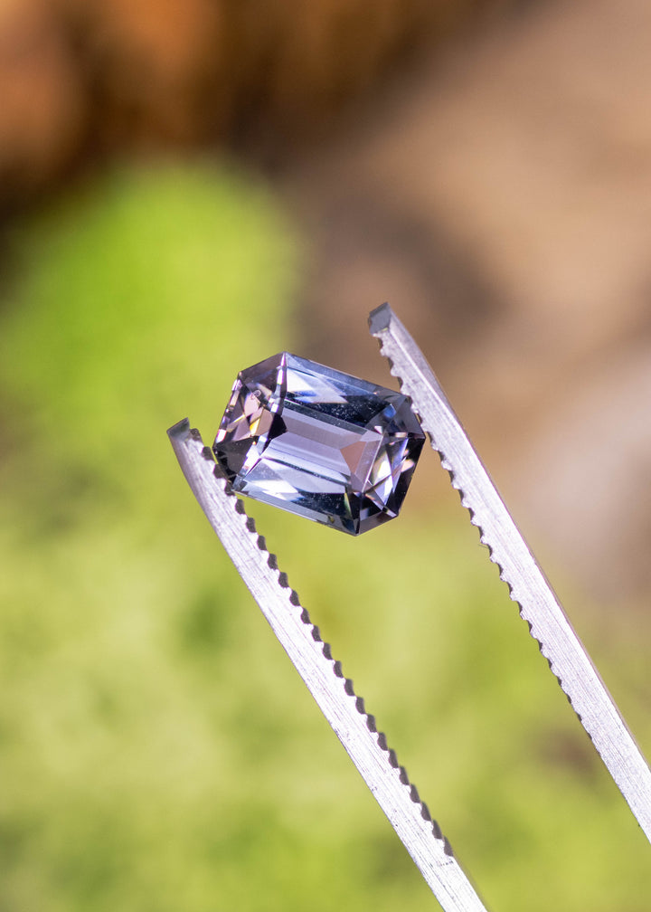 1.56 carat purple champagne teal Tanzanite modified radiant cut held in tweezers, precision faceted gemstone from Merelani Hills Arusha Tanzania displaying sharp facet junctions, mirror-like reflections and designer rectangular geometry