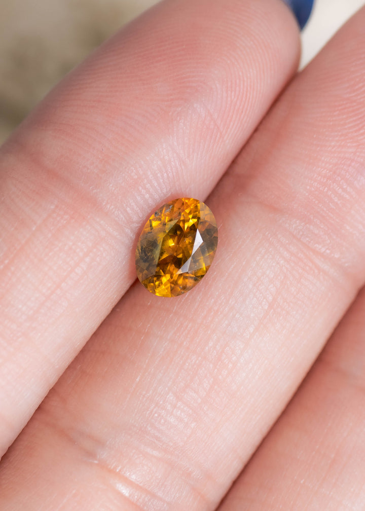 1.56ct heated yellow orange Montana sapphire resting on fingertip for scale displaying oval mix cut brilliance and warm golden orange tones from El Dorado Bar Deposit