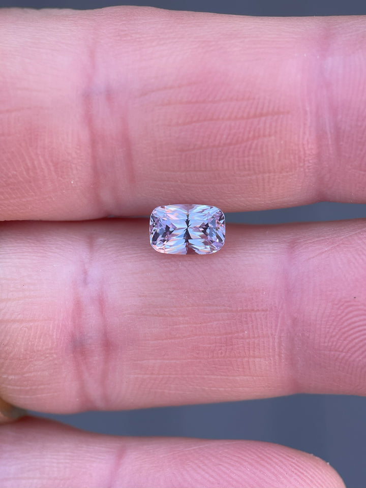 Hand-held view of a 1.57-carat purple and pastel pink rectangular cushion sapphire, showcasing its brilliant mixed cut design from Sri Lanka.