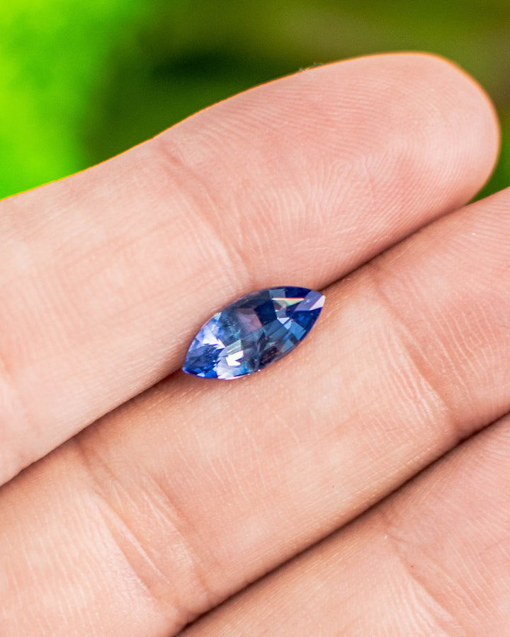 1.57 carat vivid blue sapphire displayed on fingertip in natural light, showcasing its brilliance and deep hue in a precision marquise mixed cut, untreated sapphire from Sakaraha, Madagascar.