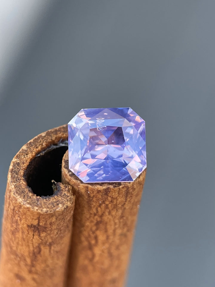 Close-up of a 1.57 carat custom radiant cut sapphire, showcasing opalescent pink and purple hues against a natural backdrop.