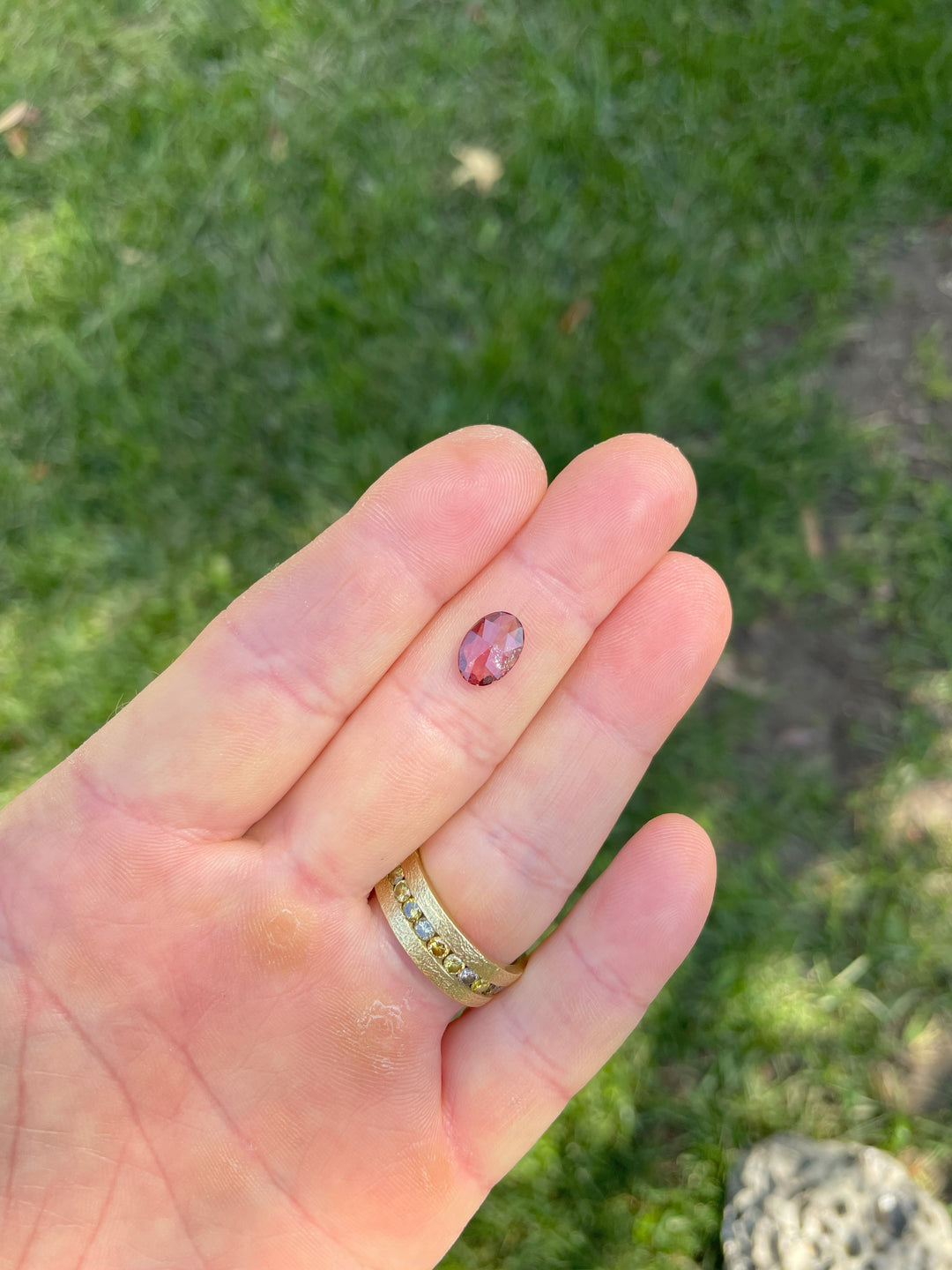 Hand displaying a 1.57-carat oval cut sapphire with orange, red, and ruby tones from Umba River, Tanzania.