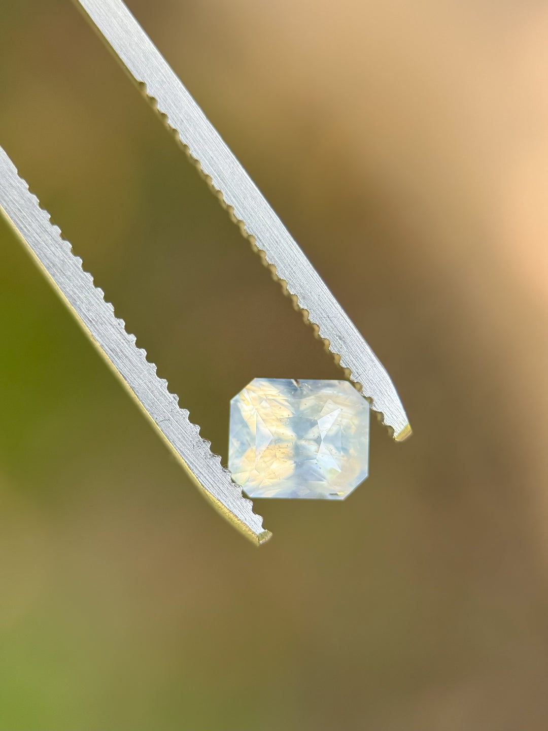 1.58 carat opalescent sapphire held in precision tweezers showcasing its radiant cut and silver-blue glow