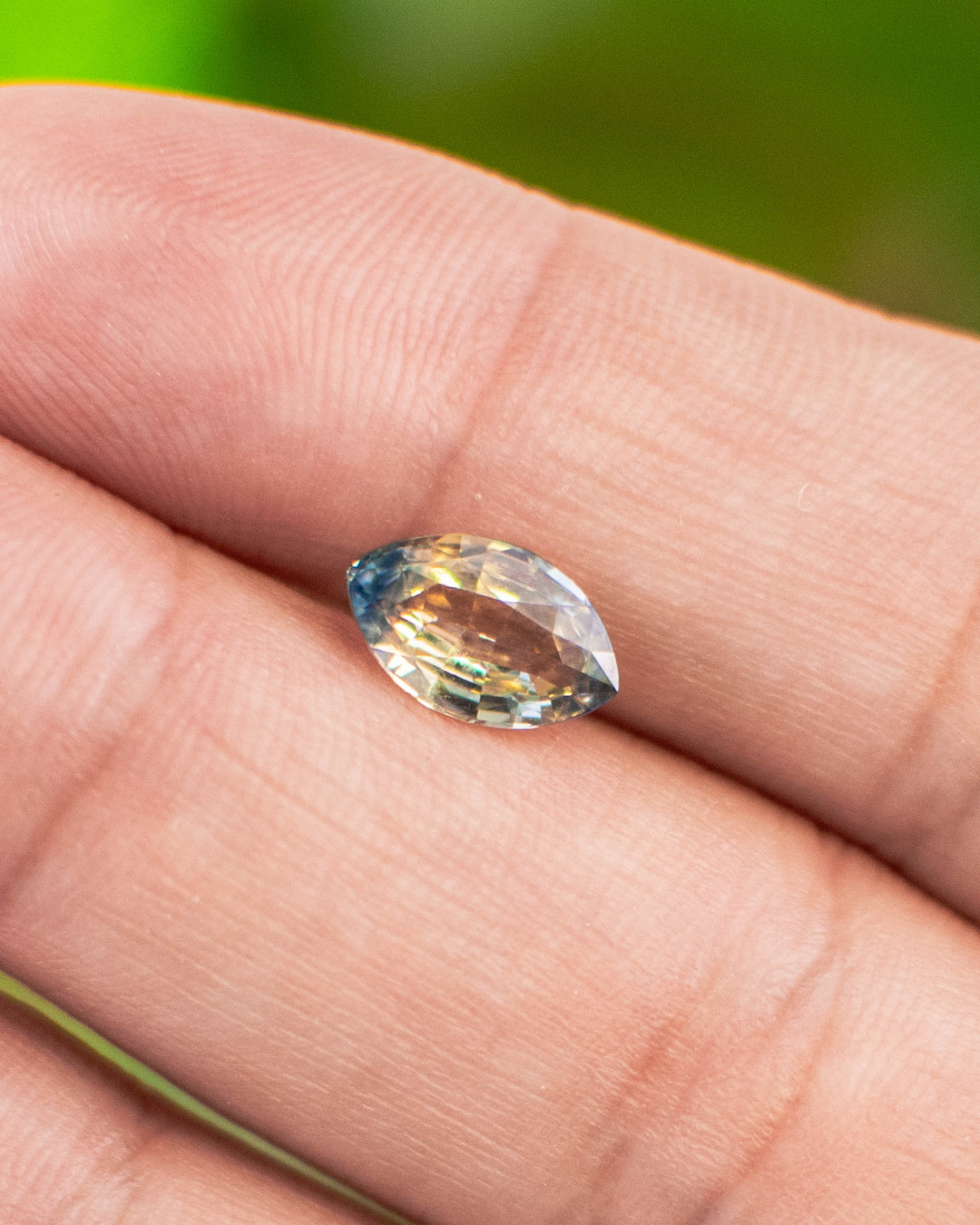 Close-up of 1.58CT parti sapphire resting on fingertip, revealing yellow and blue color zoning with exceptional brilliance and clarity, ethically sourced untreated sapphire from Sakaraha, Madagascar.
