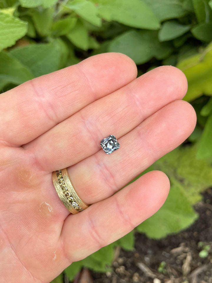 A 1.58-carat custom cut sapphire from Montana in a steely sage grey green hue, held in hand to show size and brilliance.