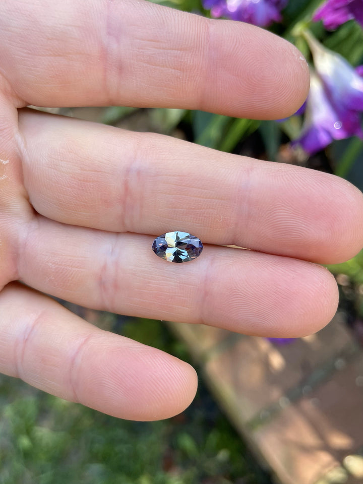 Hand holding a 1.58-carat unheated Tanzanite in a custom geometric oval cut, showing teal, gray, and purple mermaid hues.