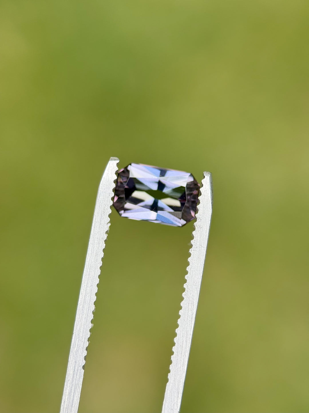 Close-up of 1.59CT antique-style octagon radiant Tanzanite in tweezers, showing green, blue, and violet mermaid hues