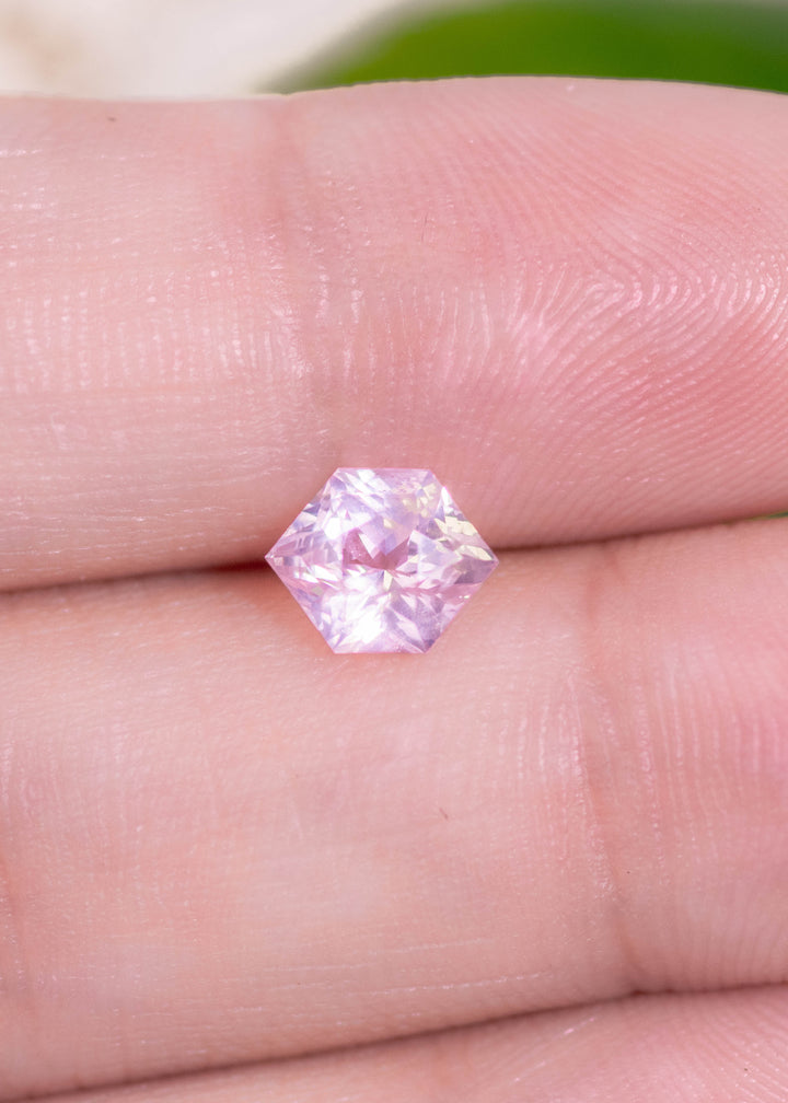 Precision cut hexagonal sapphire laid on fingers for reference of size. Bright baby pink with opalescence.