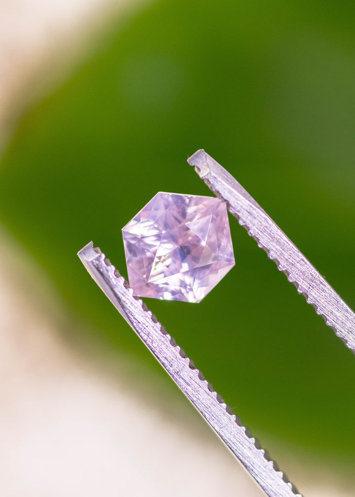 Pink opalescent hexagonal sapphire from Sri Lanka held in gem tweezers over bright green background