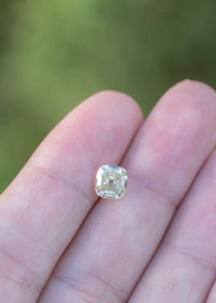 1.60 carat yellow antique-style cushion diamond resting on fingertips for scale, highlighting its square cushion outline, warm body color, and precision faceting.