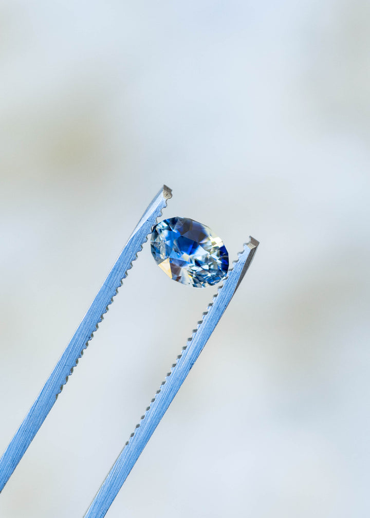 1.60ct blue and white bi color parti sapphire from Sri Lanka held in gem tweezer under natural light.