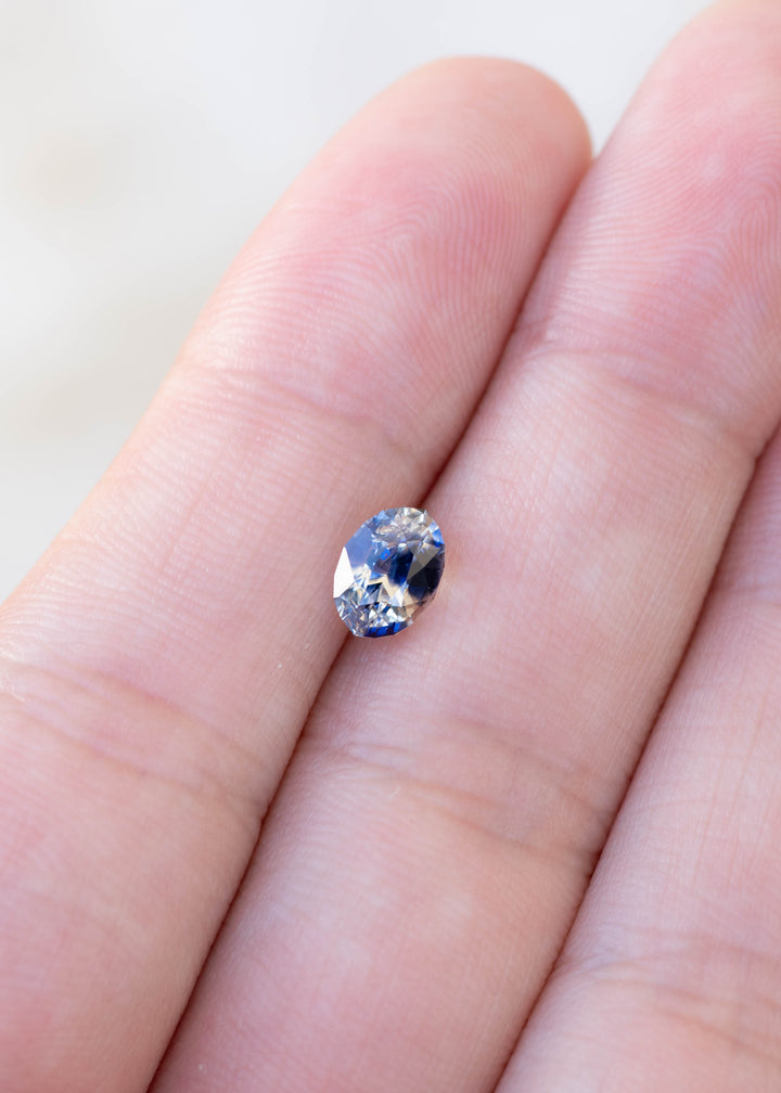 1.60ct blue and white bi color parti sapphire from Sri Lanka held in finger tips to show colors and scale.