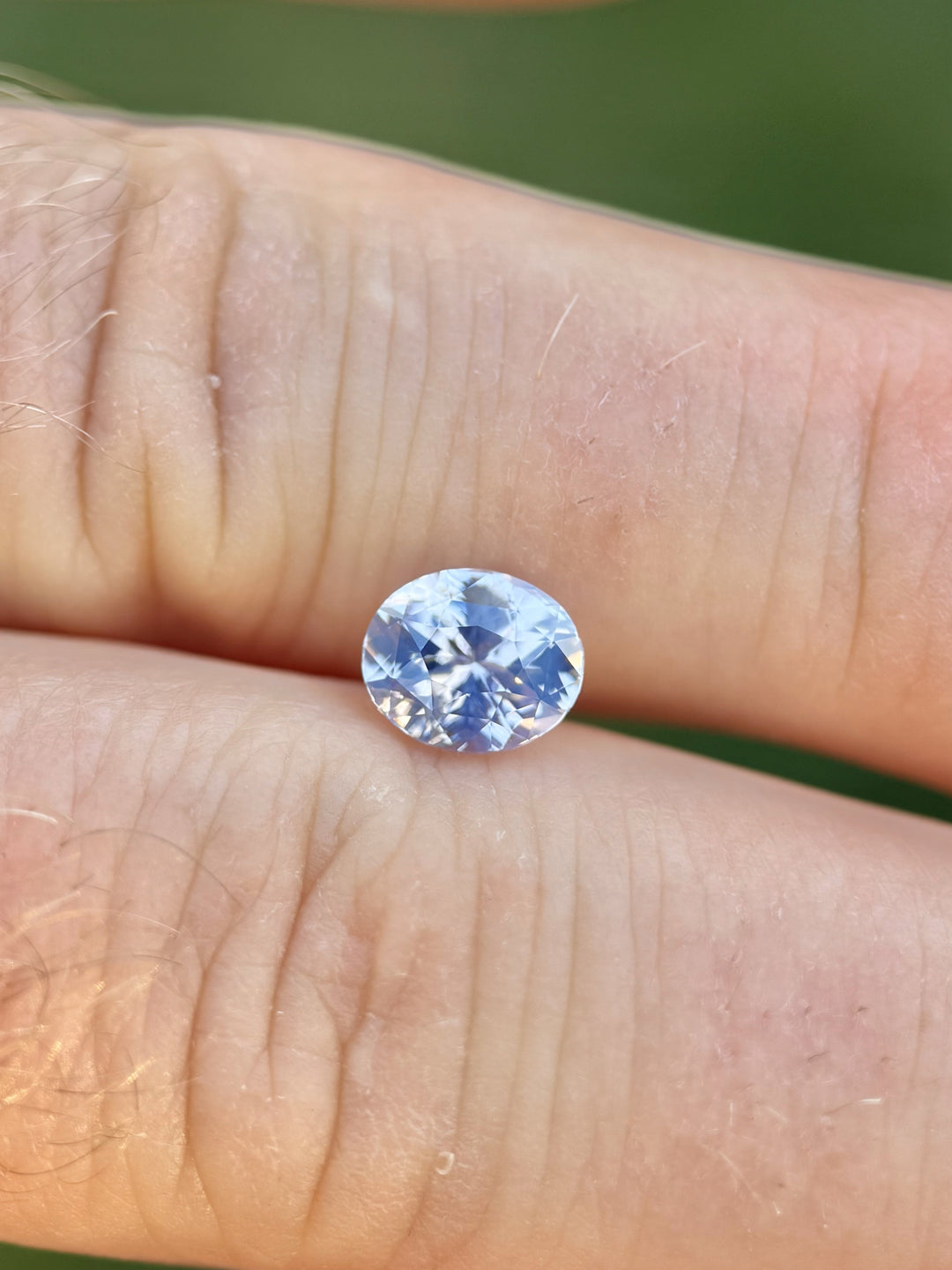 Hand holding a 1.60-carat blush, platinum, and lavender opalescent sapphire in a mix cut oval shape from Ratnapura, Sri Lanka