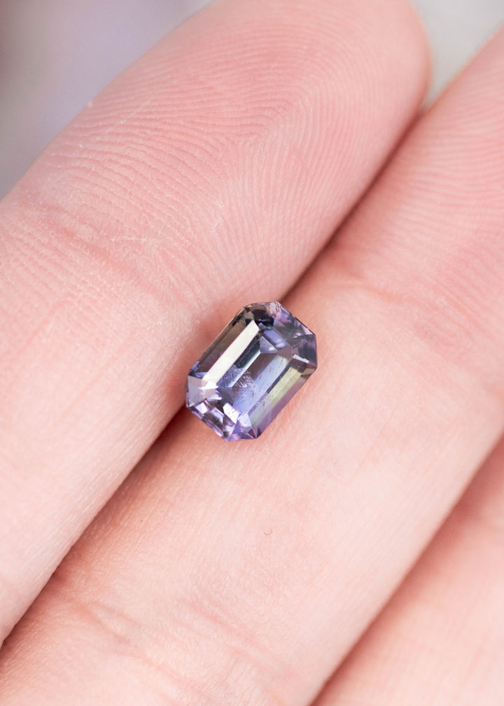1.60 carat teal green purple Tanzanite emerald cut resting on finger, untreated gemstone from Merelani Hills Tanzania showing crisp step cut faceting, elongated shape and natural color shift for custom jewelry