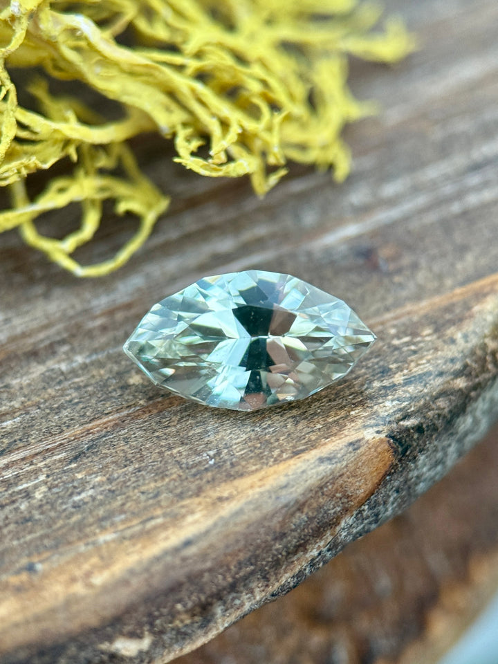 1.61 carat yellow sapphire resting on rustic wood near golden moss, showing warm golden tones and crisp facet reflections in a precision marquise mixed cut, untreated sapphire from Sakaraha, Madagascar.