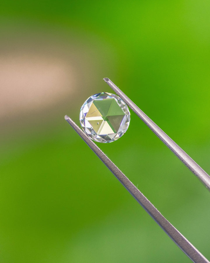 Light green 1.62 carat round modified brilliant rose cut diamond from South Africa held in tweezers. The GIA certified stone showcases a flat rose-style top and SI2 clarity with delicate brilliance.