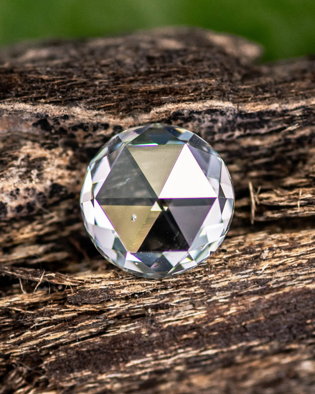 Close-up of a 1.62 carat light green round modified brilliant rose cut diamond from South Africa resting on natural wood. The GIA certified SI2 clarity stone shows a laser-drilled inclusion and organic sparkle under natural light.