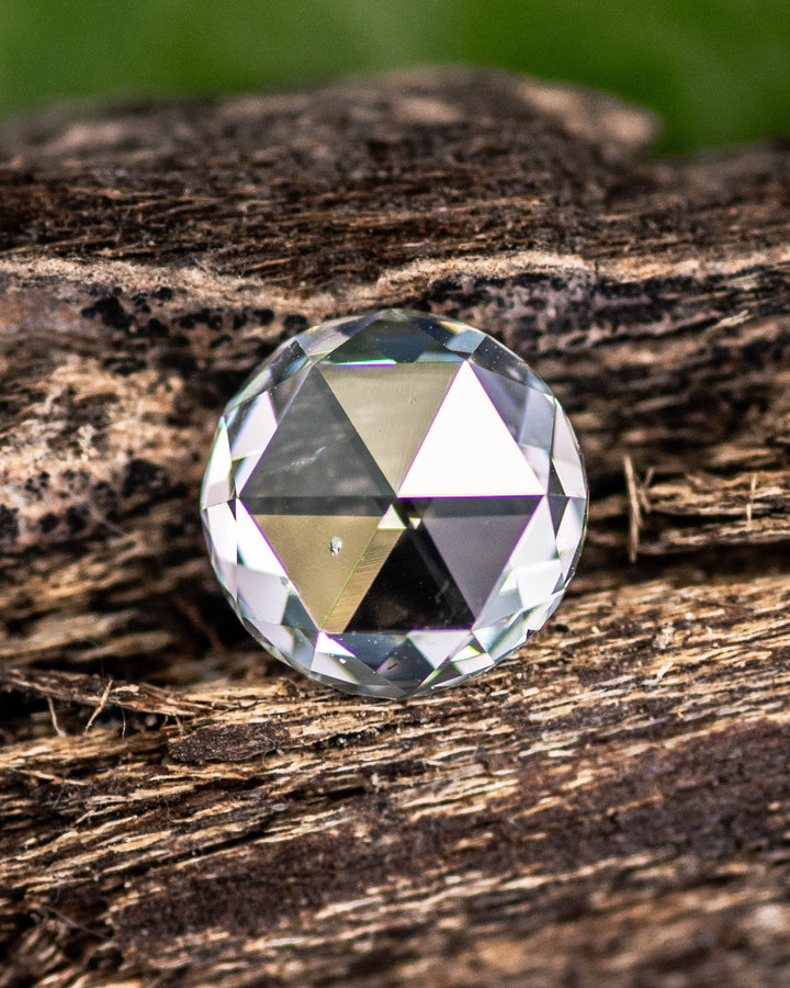Close-up of a 1.62 carat light green round modified brilliant rose cut diamond from South Africa resting on natural wood. The GIA certified SI2 clarity stone shows a laser-drilled inclusion and organic sparkle under natural light.