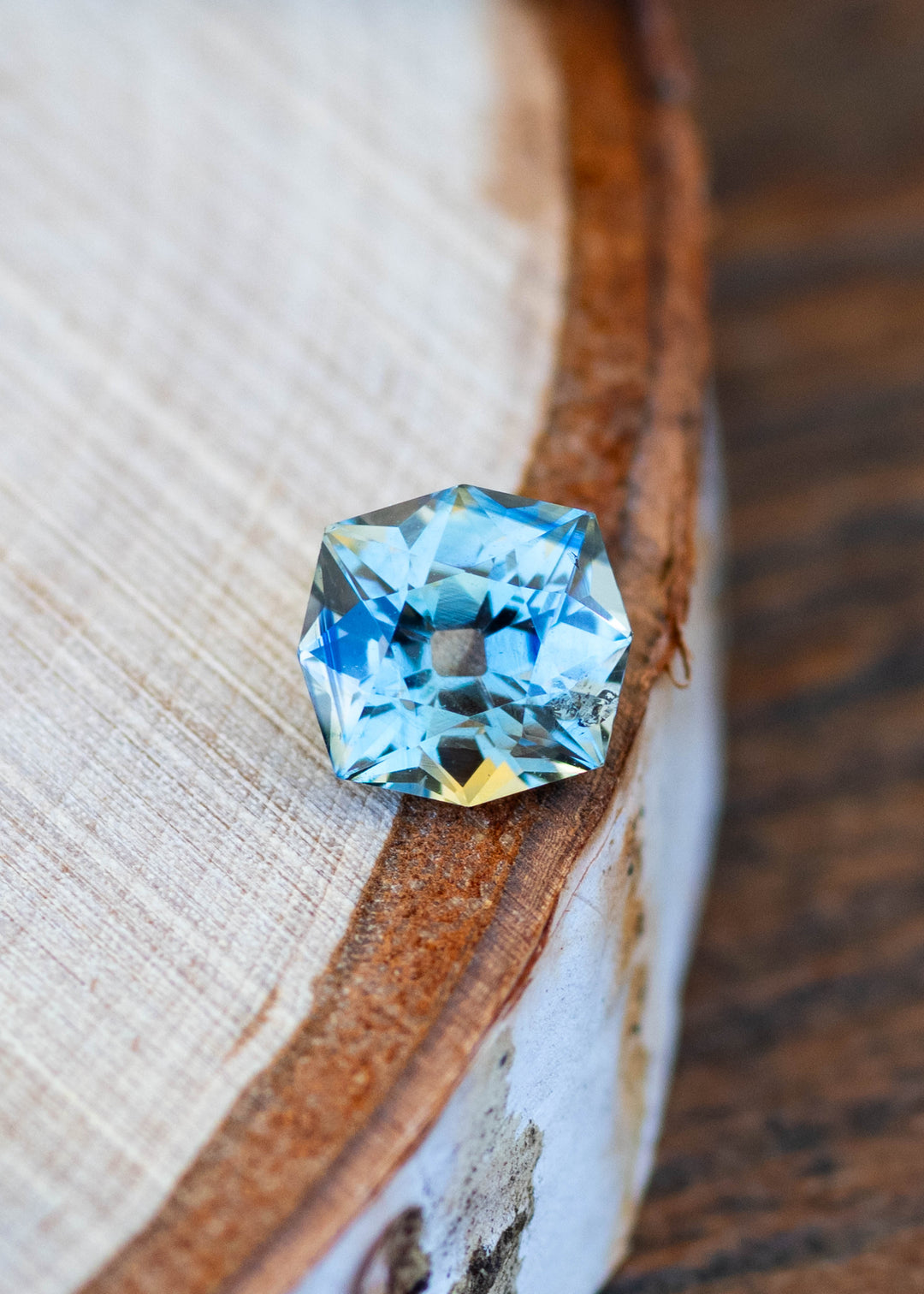1.62ct teal yellow parti custom old mine cushion cut sapphire resting on the edge of a slice of wood under natural lighting.