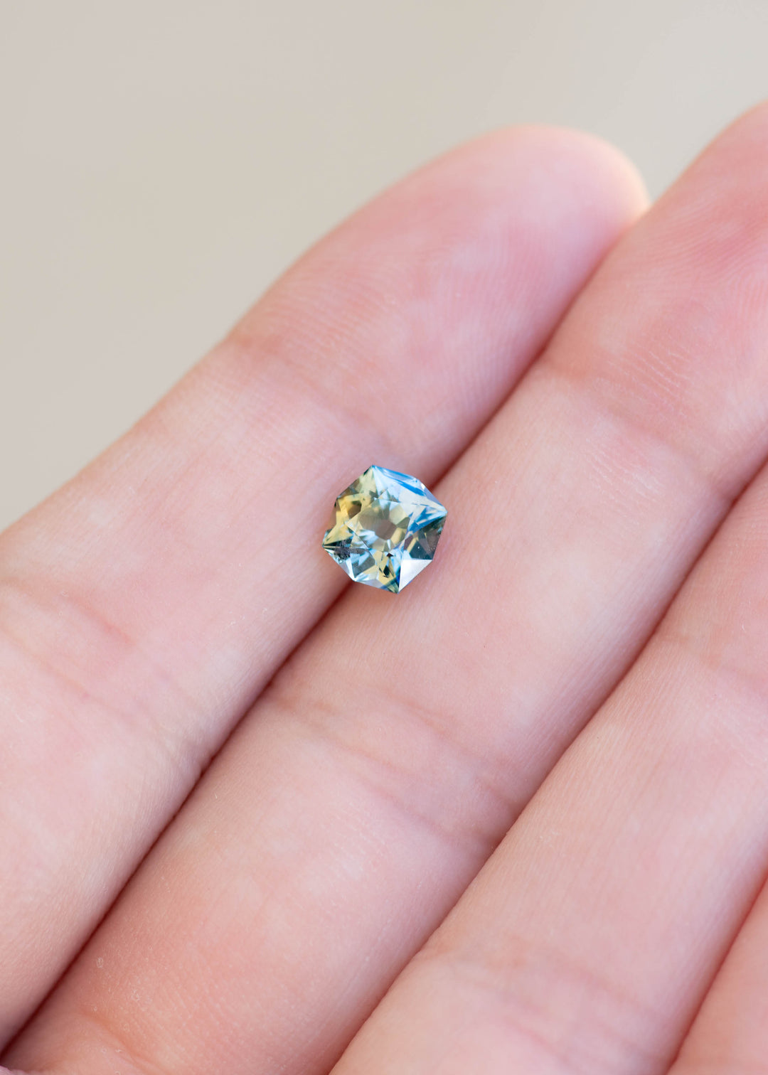 1.62ct teal yellow parti custom old mine cushion cut sapphire held in finger tips to show off color, cut, and scale.
