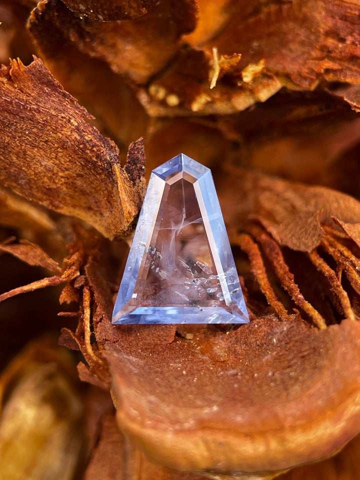 A 1.62-carat unheated sapphire with powder blue and denim blue hues, featuring a custom geometric portrait cut. Ethically sourced from Sri Lanka and displayed against a natural textured background.