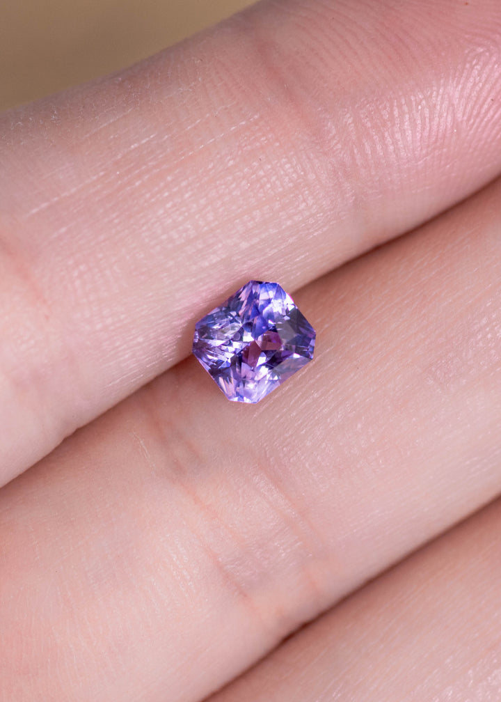 Loose purple pink sapphire resting on fingertips, showing the radiant cut facet pattern and natural color saturation from Sakaraha, Madagascar.