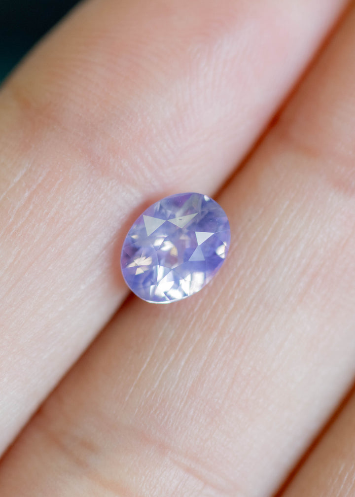 Unheated oval mix cut sapphire resting on fingertips, revealing opalescent pink and purple tones with balanced symmetry.