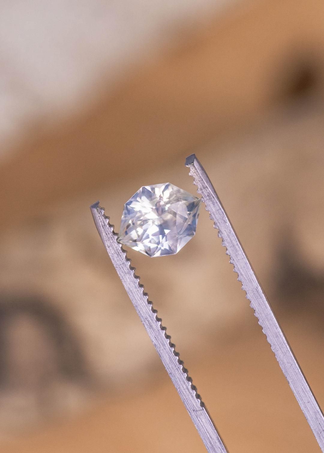 Loose pastel green and yellow sapphire from Sri Lanka held in tweezers showing the custom geometric marquise cut and soft pastel color tones.