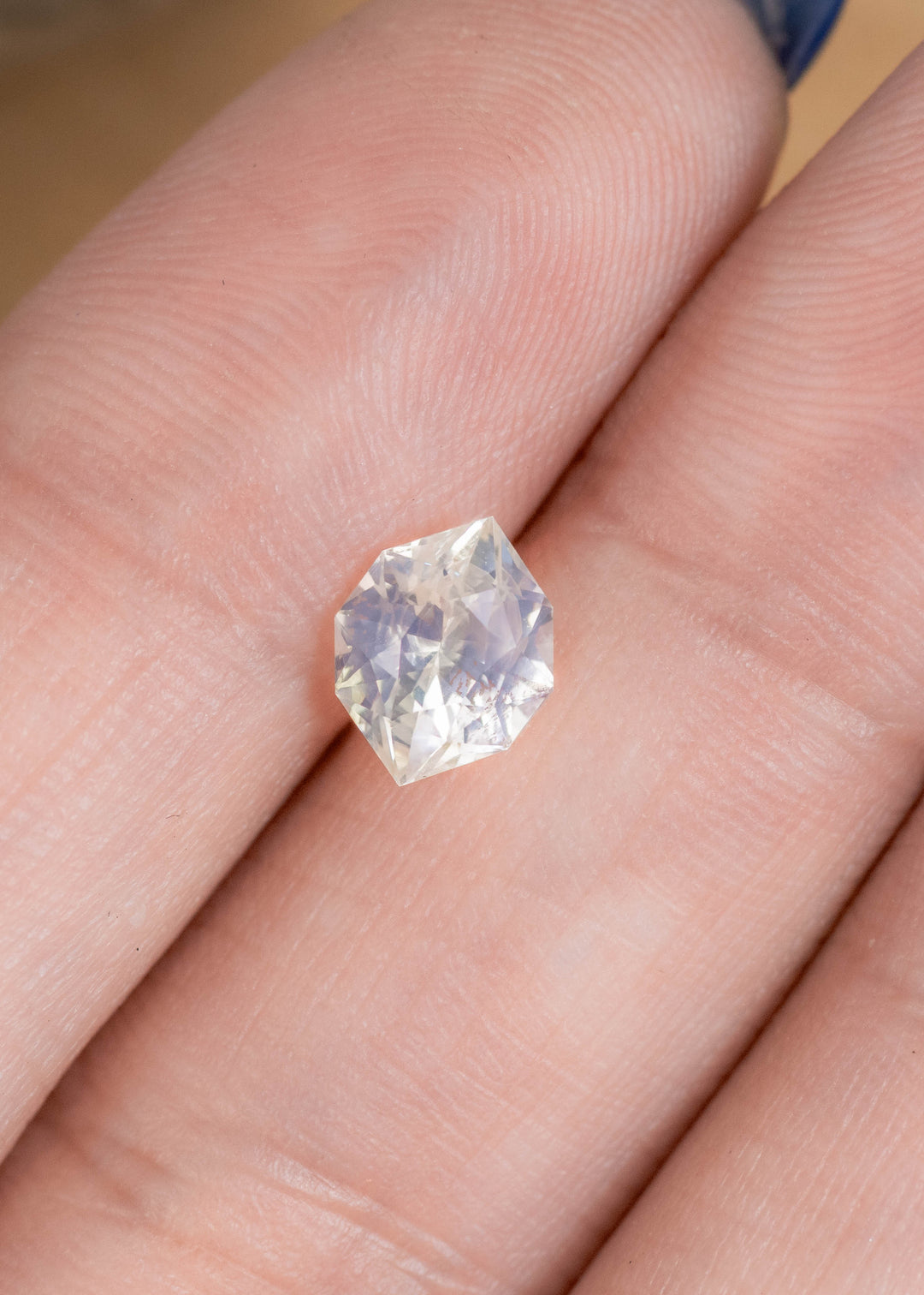 Loose pastel green yellow sapphire from Ratnapura Sri Lanka resting on fingertips displaying the custom geometric marquise cut and natural color shift.