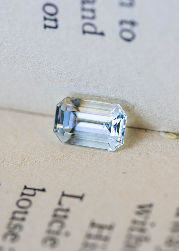 Untreated 1.63 carat pale blue aquamarine from Colorado displayed on a vintage book, highlighting its custom emerald cut and exceptional transparency.