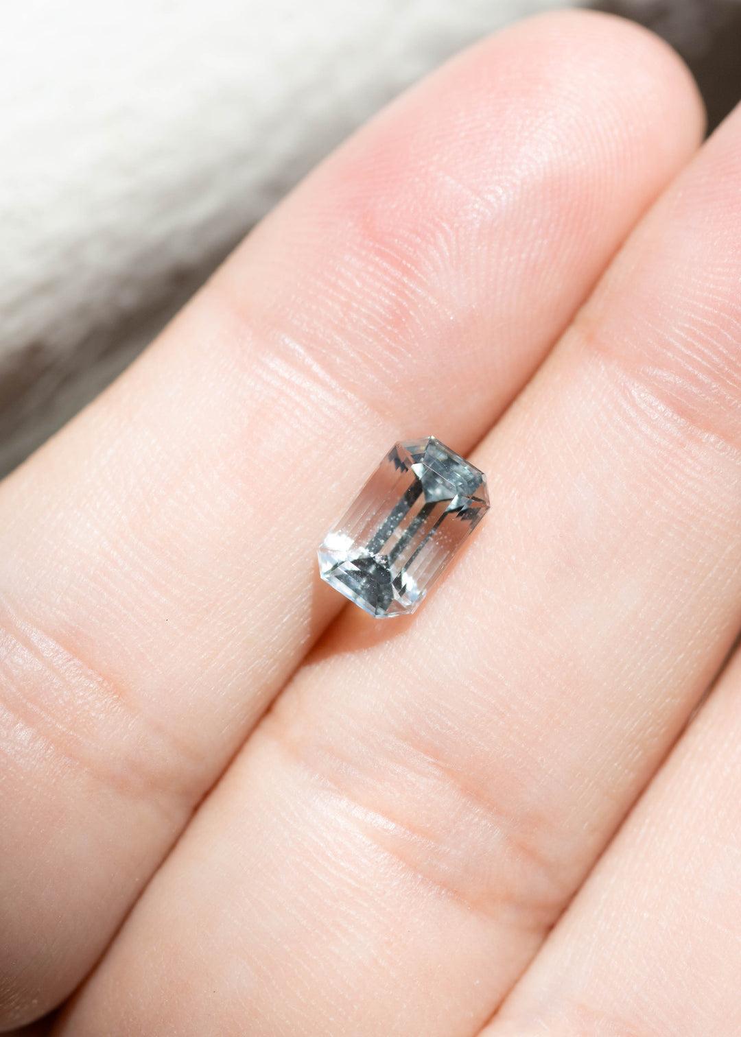 Natural untreated pale blue Colorado aquamarine resting on fingertips, showcasing its elongated custom emerald cut and face-up size.