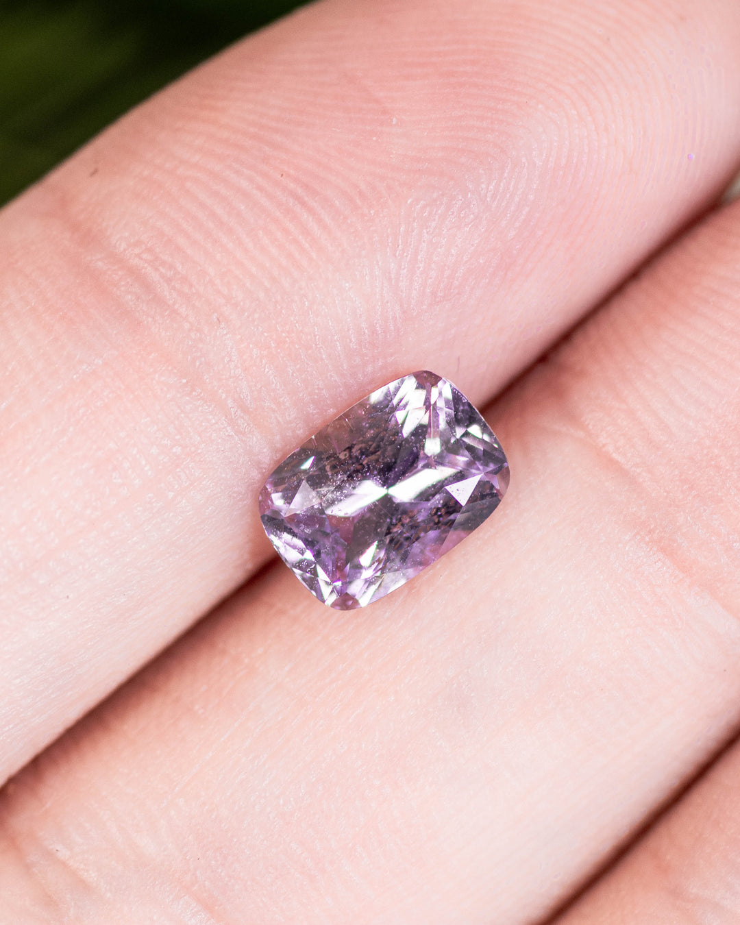 1.65 carat multicolor violet, purple, and pink sapphire resting on fingertips under natural light, showcasing the play of colors and precision of the cushion brilliant cut, untreated gemstone from Sakaraha, Madagascar.