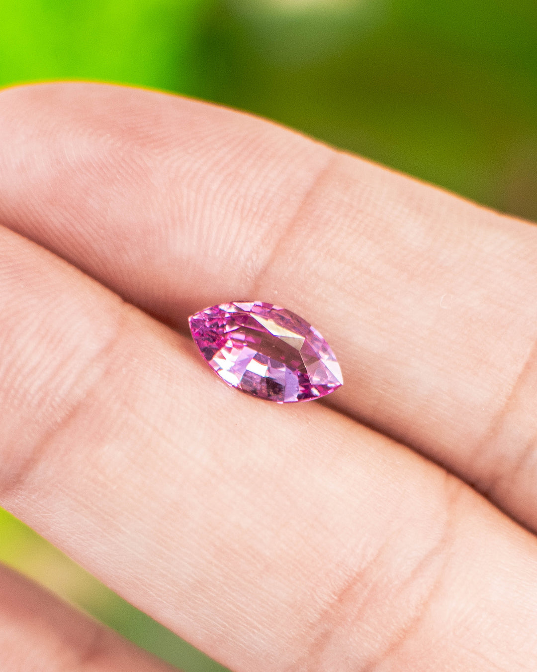 1.65 carat hot pink sapphire resting on fingertips under natural light, revealing vibrant magenta tones and lively brilliance of the precision marquise mixed cut, untreated sapphire from Sakaraha, Madagascar.