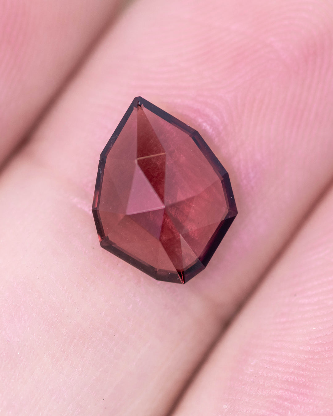 1.66 carat red and orange garnet displayed on fingertips, revealing depth of color and transparency through the custom geometric rose cut shield, untreated garnet from Kenya.